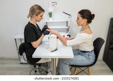 Manicurist paints the nails of a young girl with red varnish in a beauty salon. Side view. Nail care concept.