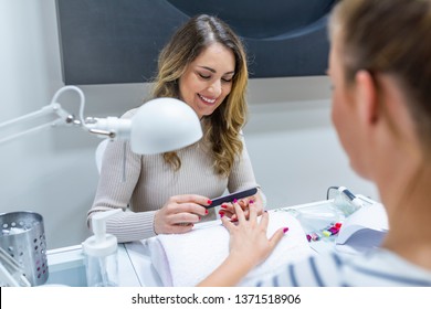 Manicurist performing a professional manicure. Manicurist performing a professional manicure. Friendly nail technician applying a product on customers hands - Powered by Shutterstock