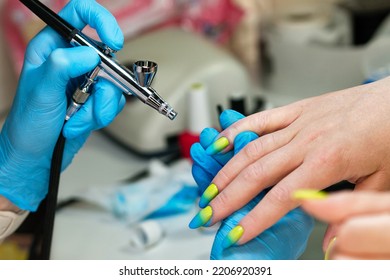 Manicurist using airbrush to paint fingernails female client in nail salon. Master does design nails with airbrush. Woman customer getting nail manicure. Process procedure for spraying paint on nails