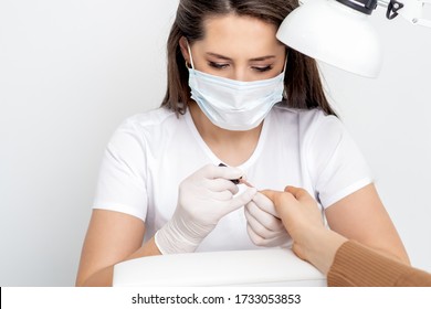 Manicurist Wearing Protective Mask Painting Female Nails With Nail Polish In Manicure Salon.