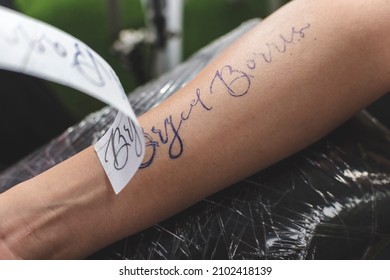 Manila, Philippines - Dec 2021: A Professional Tattoo Artist Removes Carbonized Stencil Paper Revealing The Outline Of A Calligraphic Tattoo Design On A Client's Forearm.