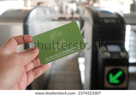Manila, Philippines: hand holds Light Rail Transit 1 Single Journey Ticket in front of tap machines. Close-up of one-time use contactless LRT Line 1 smart card in train station. Public transportation.