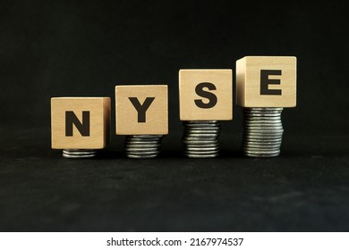 Manila, Philippines - June 13, 2022 : NYSE in wooden blocks with increasing stack of coins in black background. United States US stock market economy growth and recovery concept. 