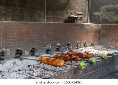 Manila, Philippines - March 5, 2019: Calavite street in Salvacion part of town. Three piglets on spits, called Lechon Baboy, are still roasting over burning ash heap in large open pit under roof.