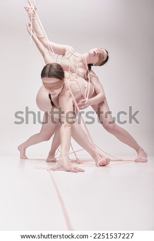Manipulator. Portrait of two young girls posing in underwear and ropes with eyes closed over light studio background. Concept of modern fashion, queer art photography, weird people, creativity