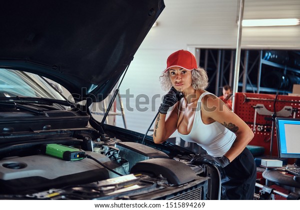 Manly strong woman is fixing car\'s engine with\
computer help at auto\
service.