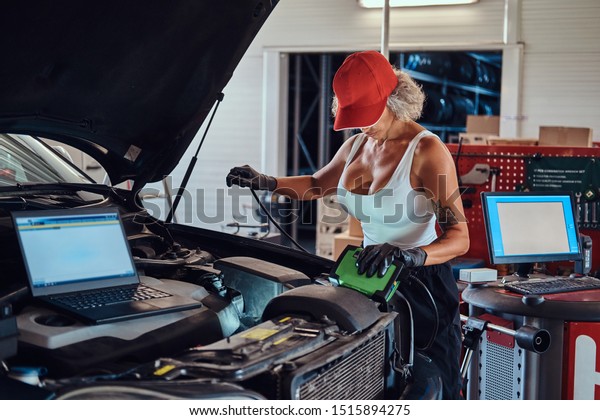 Manly strong woman is fixing car\'s engine with\
computer help at auto\
service.