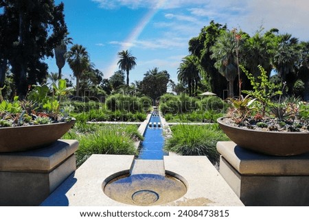 a manmade concrete stream in the center of a park surrounded by lush green trees and plants and colorful flowers and a rainbow at Huntington Library and Botanical Gardens in San Marino California USA