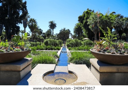 a manmade concrete stream in the center of a park surrounded by lush green trees and plants and colorful flowers at Huntington Library and Botanical Gardens in San Marino California USA