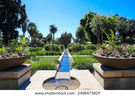 a manmade concrete stream in the center of a park surrounded by lush green trees and plants and colorful flowers at Huntington Library and Botanical Gardens in San Marino California USA
