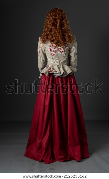 A mannequin with long red hair wearing an embroidered\
renaissance-style bodice and red skirt shown from behind\
