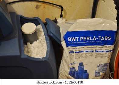 Mannheim, Germany-10.16.2019: Open bag of water softener salt beside the open gray brine tank full of water softener salt pellets
