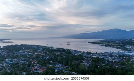 Manokwari city, West Papua, Indonesia. A serene aerial view showcases a coastal town nestled by the calm sea, framed by distant mountains under a vast, cloudy sky. - Powered by Shutterstock