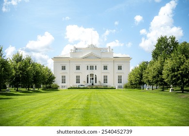 Užutrakis Manor, a neoclassical mansion near Trakai, Lithuania, stands elegantly with its white facade, surrounded by lush lawns and lined with trees, offering a serene and picturesque landscape. - Powered by Shutterstock