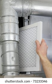 A Man's Arm And Hand Seen Replacing Disposable Air Filter In Home Central Air Furnace.