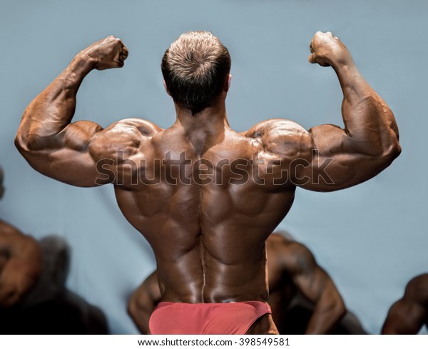 Man's back double biceps pose. Bodybuilder demonstrating arms on stage ...