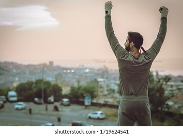 The man's back view in a suit celebrates the victory. While training with his hands up he looks at the city.