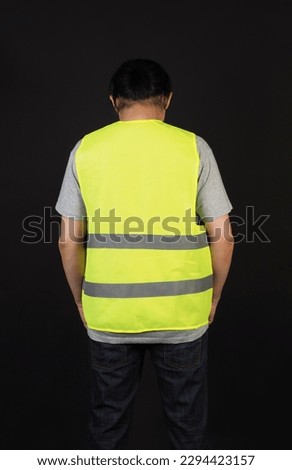 The man's back wears Safety Vest and a grey T-shirt on black background.