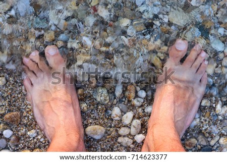 Man's Bare Feet Sank in the Water on the Rocky Beach