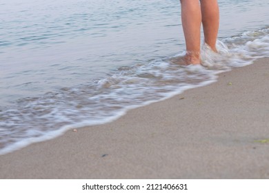 Man's bare feet stepping on calm seashore foamy wave and wet sand by evening, enjoying life and nature. Summer holiday, relaxing travel or mindfulness meditation to the sounds of the ocean concept.