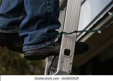 mans black shoes standing on silver ladder with christmas lights