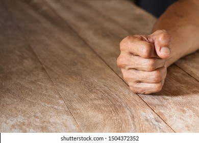 Man's clenched fist on vintage wooden table - Shutterstock ID 1504372352