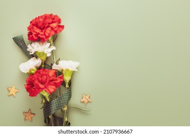 Mans Day holiday card with red and white carnations with gift ribbon and wooden stars on a green background with copy space for congratulatory text suitable for 23 february, 9 may or fathers Day - Shutterstock ID 2107936667