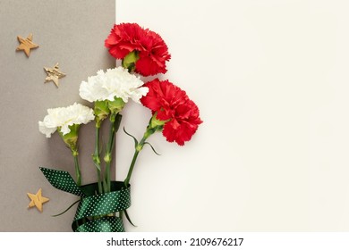 Mans Day holiday card with red and white carnations with gift ribbon and wooden stars on a white background with copy space for congratulatory text suitable for 23 february, 9 may or fathers Day