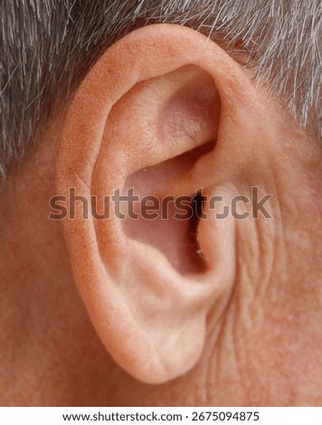 A man's ear is visible with a small amount of hair. The ear is pink and has a small amount of hair on it
