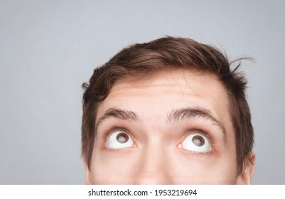 Man's Eyes Looking Up On The Light Background. Empty Place For A Text Or Object. Close-up Shot Of Shocked Young Man With Round Eyes, Top Half Head. Eyes Looking On Top
