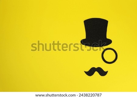 Man's face made of fake mustache, hat and monocle on yellow background, top view. Space for text