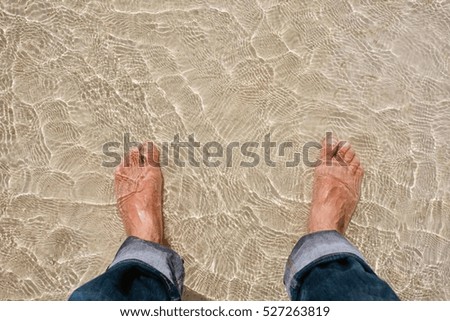 Mans feet in clear water on beach