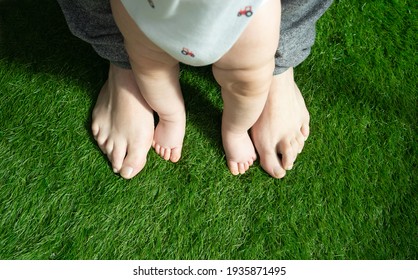 man's feet next to baby's feet on artificial grass. first steps parenting concept