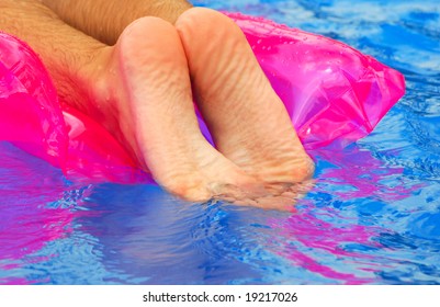 Man's Feet Relaxing On Floatie In Pool