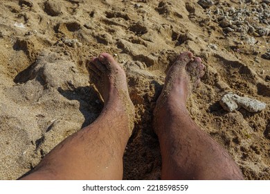 Man's Feet Sunbathing On White Sand On The Beach.