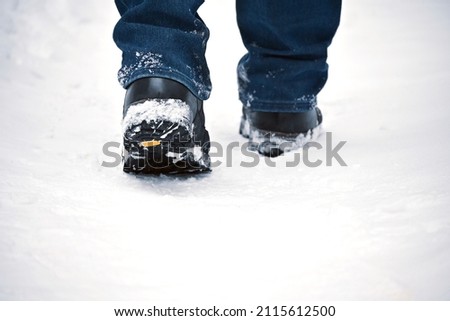 A man's feet in winter warm, comfortable shoes take a step on a snowy road in the park on a winter walk. A man in motion.  