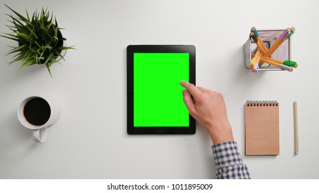 A Man's Finger Scrolling On The Green Touchscreen. A Tablet Is On The White Table. View From The Top. Close-up.