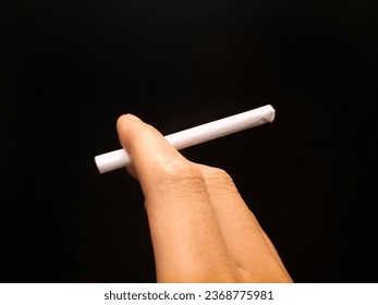 Man's fingers holding cigarette on isolated black background. - Shutterstock ID 2368775981