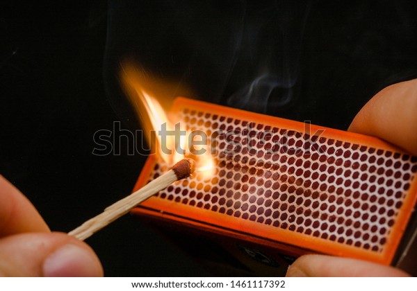 Man\'s fingers lighting a match, rubbing against the\
matchbox, setting fire to friction. On a black background. Matches\
and fire.