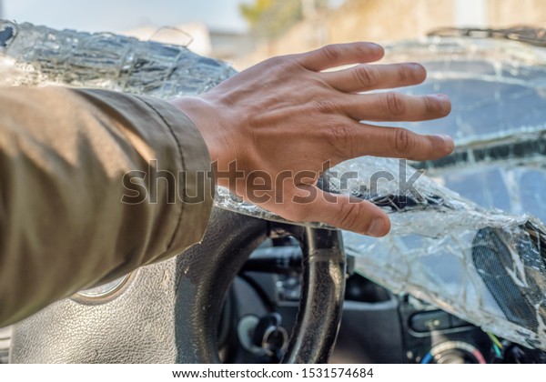 A man\'s fist against the\
broken windshield. Cracks on the windshield of the car from the\
impact
