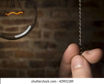 A man's hand is about to switch off the bulb light. Brick wall as background. - Powered by Shutterstock