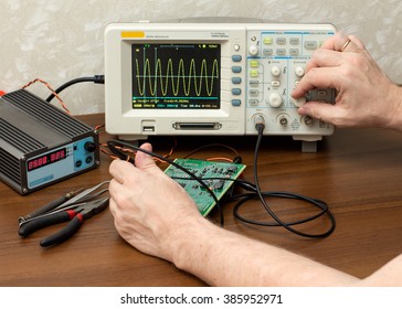 Man's hand adjusts the amplitude of the sine wave on an oscilloscope - Shutterstock ID 385952971