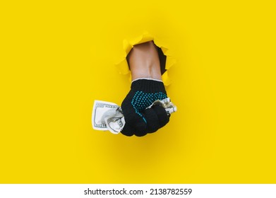 A man's hand in a black fabric work glove holds dollar bills (money). Torn hole in bright yellow paper. Concept for gastarbeiter, handyman, salary for job. Copy space.