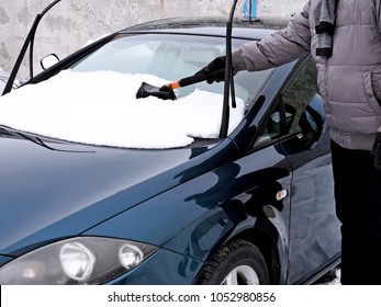 Man's hand with a brush cleans snow on the hood of the car