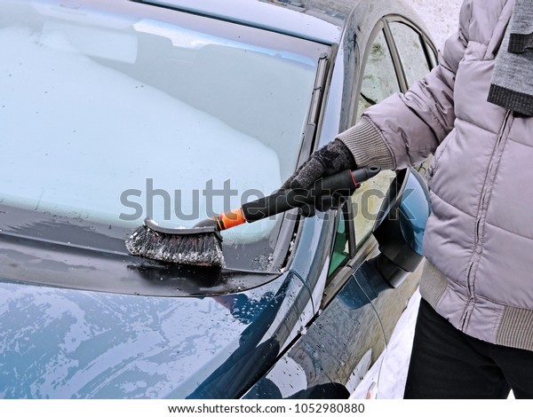 Man\'s hand with a brush cleans snow on the hood of\
the car