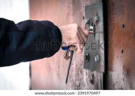 A man's hand with a bunch of keys opens a rusty garage door. Close up.