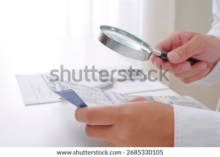 A man's hand checking insurance documents with a magnifying glass
