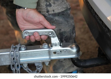 A man's hand checks the fixation of the trailer closed hitch lock handle on the towing ball towbar of the car closeup, the safety of driving with a trailer on the road