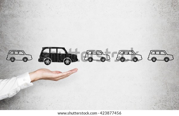Man\'s hand choosing black car\
sketch over row of white cars on concrete wall. Concept of\
choice