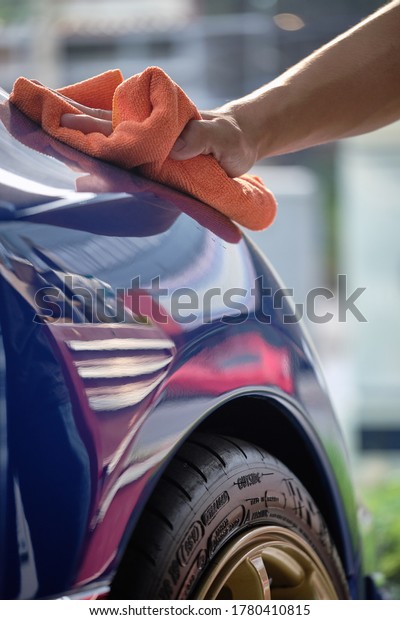 Man's hand cleaning car & drying vehicle with
microfiber cloth. Hand wipe down paint surface of shiny blue sedan
after polishing and ceramic coating. Car detailing, maintenance,
and car wash concept. 